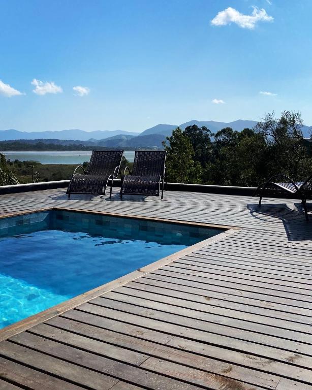 a swimming pool with two chairs on a wooden deck at Villa Mavi - Praia do Rosa in Imbituba