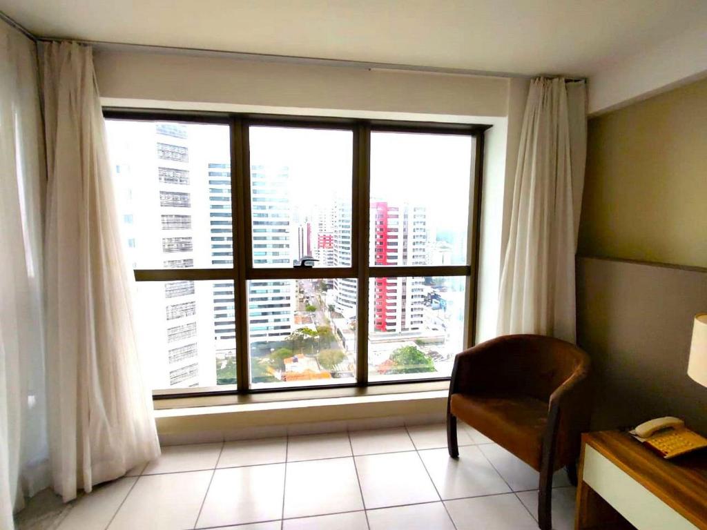 ein Zimmer mit einem großen Fenster mit einem Stuhl vor dem Zimmer in der Unterkunft Beach Class Executive - Boa Viagem in Recife