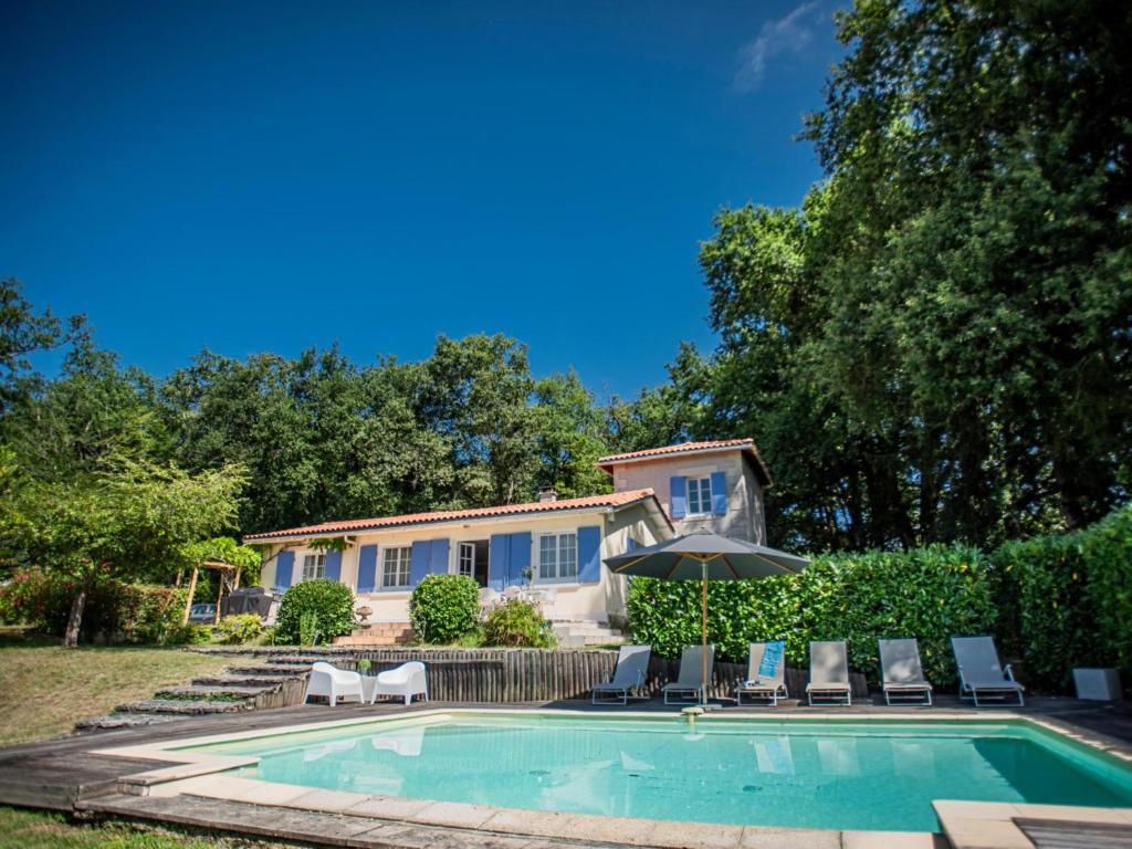 a house with a swimming pool with chairs and an umbrella at La Maison sur la Colline in Laprade