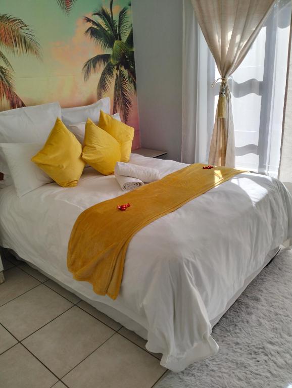 a white bed with yellow pillows and a blanket on it at O&S BnB in Centurion