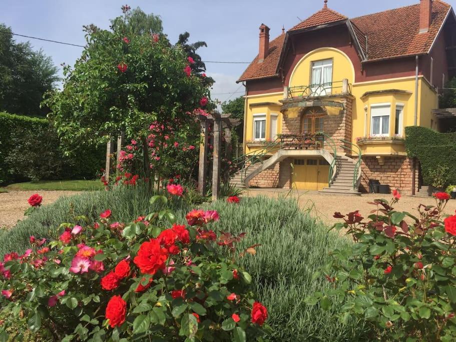 une maison jaune avec des fleurs rouges devant elle dans l'établissement Bourgogne grande maison avec jardin à la française, à Pontailler-sur-Saône