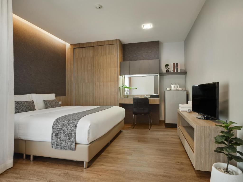 A compact studio-style room combining a double bed, work desk, kitchenette and television.