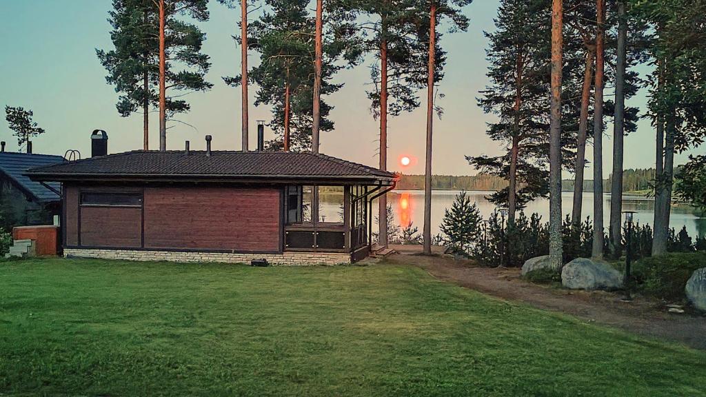 a small building in a yard next to a lake at Villa Valkama with optional beach sauna + jacuzzi in Tahkovuori