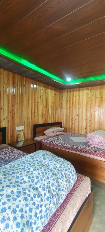 two beds in a room with wooden walls and green lights at Zero Points TheLaure Cottage in Ilām