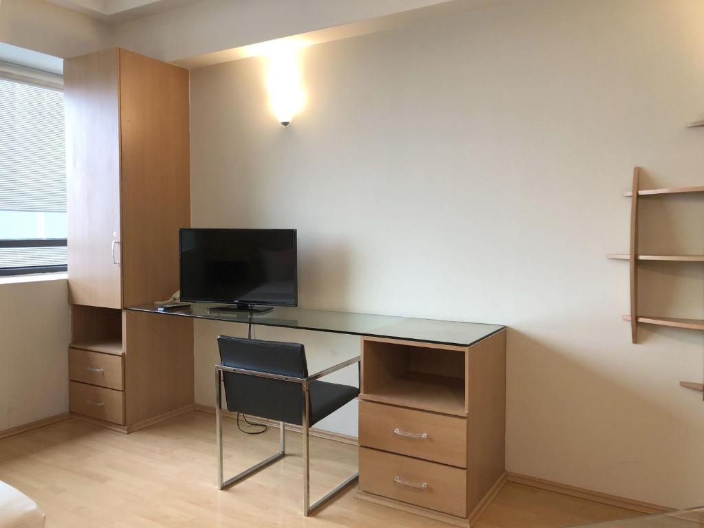 A compact glass desk with television and storage beside the apartment window.