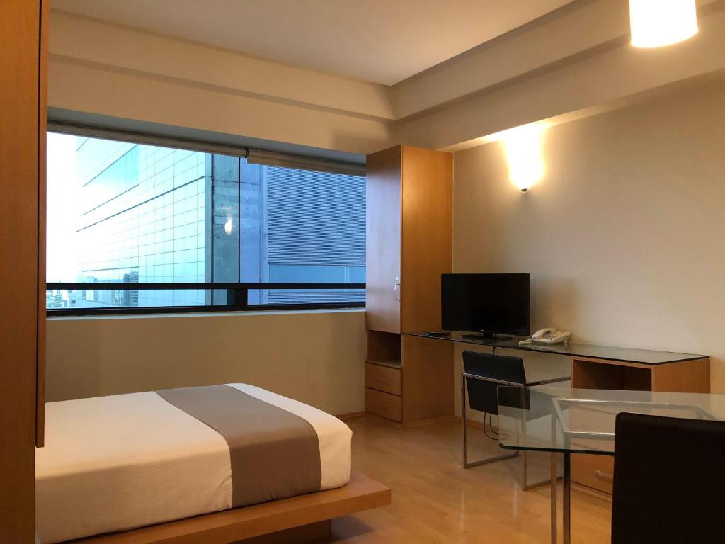 A compact modern guest room with a double bed, work desk, television and large window.