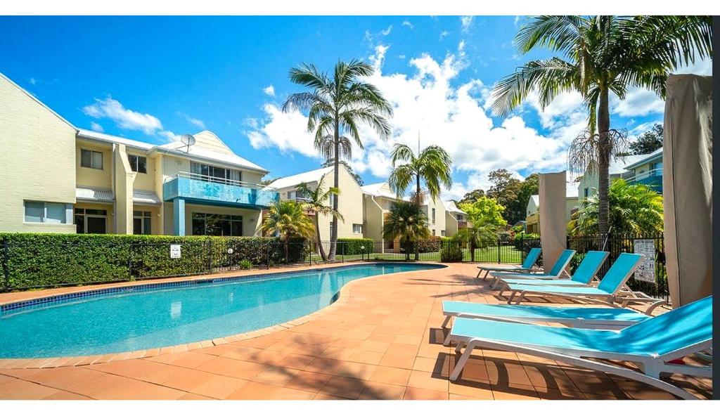 a swimming pool with blue lounge chairs and palm trees at Bec's Beach House Getaway in Batemans Bay