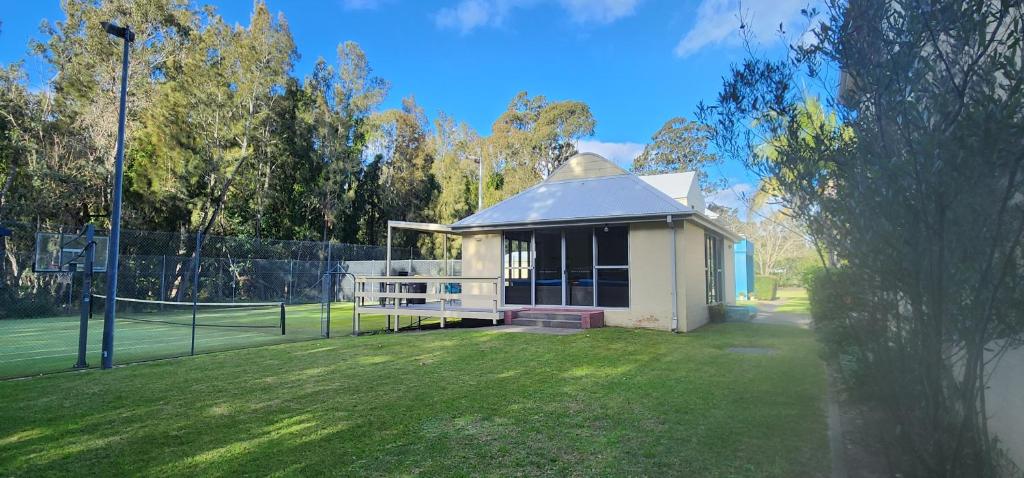 a small building in a field with a tennis court at Bec's Beach House Getaway in Batemans Bay