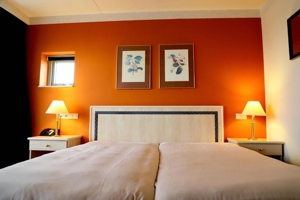 a bedroom with an orange wall with a bed and two lamps at City Hotel Restaurant Stadskanaal in Stadskanaal