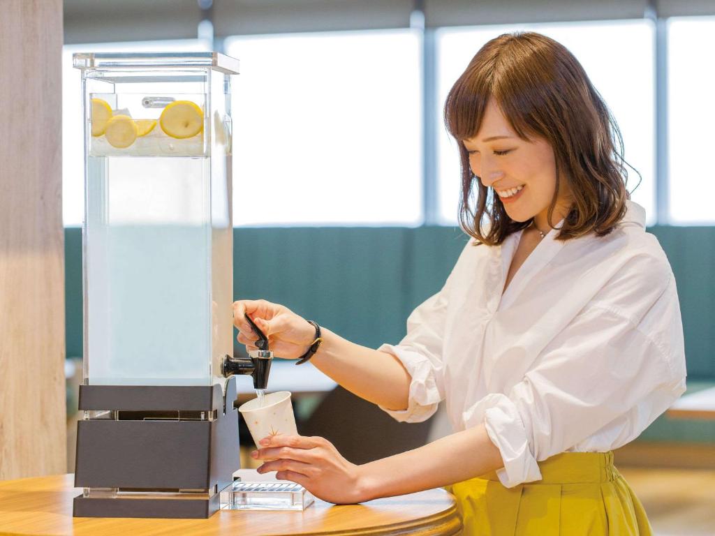 a woman is making a drink in a machine at Comfort Hotel Central International Airport in Tokoname