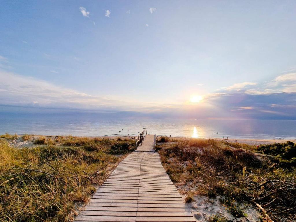 a wooden path leading to the beach with the sun setting at Rise and Shine apartment in Juodkrantė