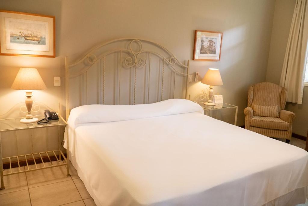 Un dormitorio con una gran cama blanca y una silla. en Vila Real Hotel, en Jaú