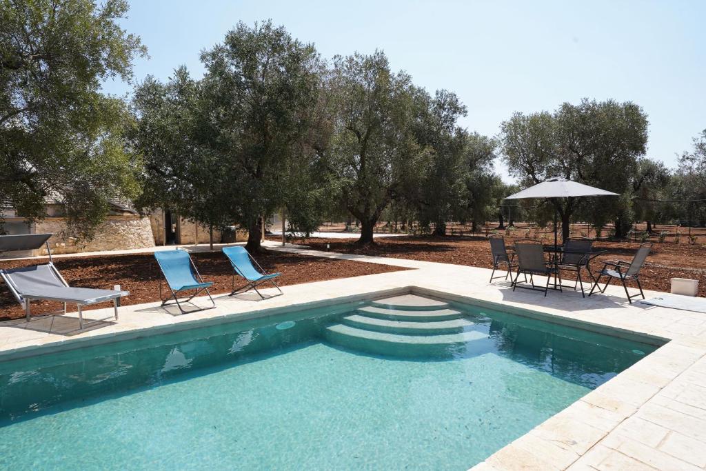 - une piscine avec des chaises, une table et un parasol dans l'établissement Trullo Le Rondinelle, à San Michele Salentino