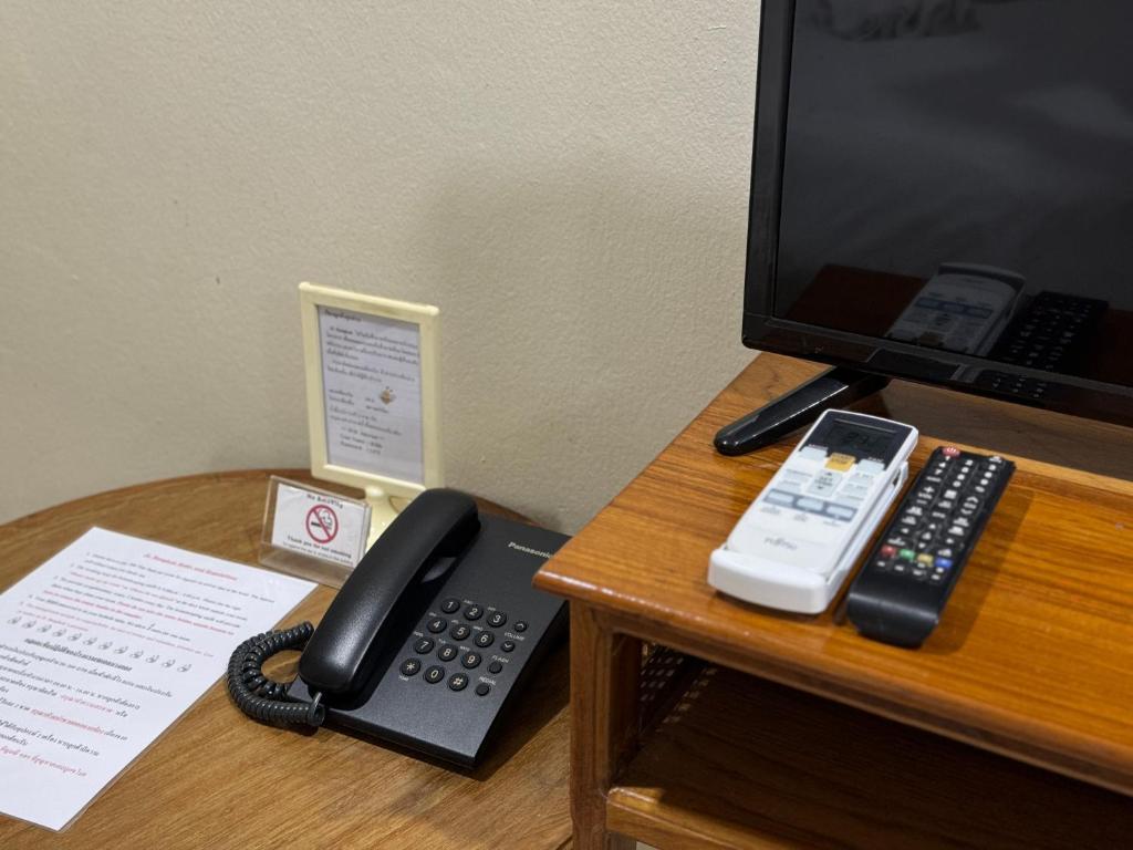 A hotel desk corner with a telephone, television remotes and an information sheet.