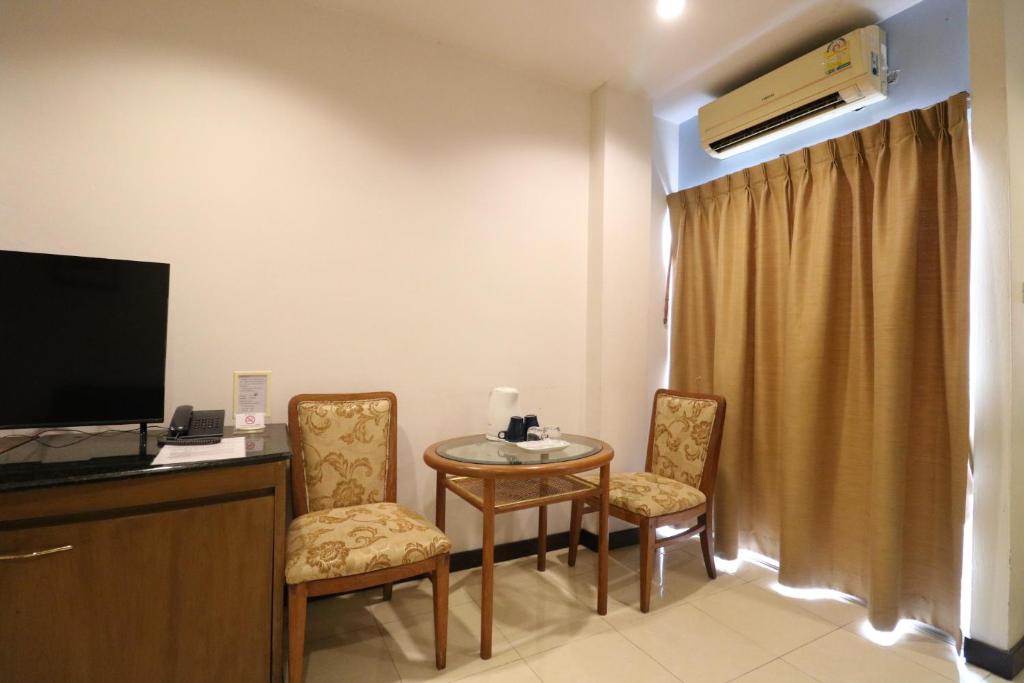 A small hotel-room sitting area with patterned chairs, a round table and a television cabinet.