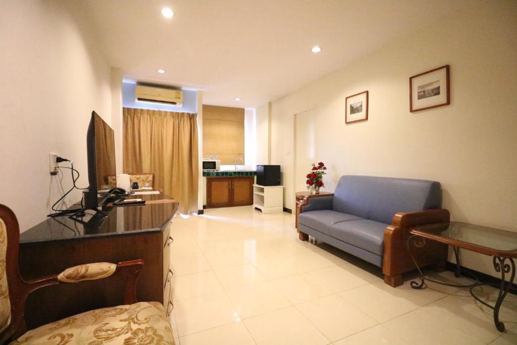 A spacious-looking living area with a blue sofa, television, dining table and kitchenette corner.