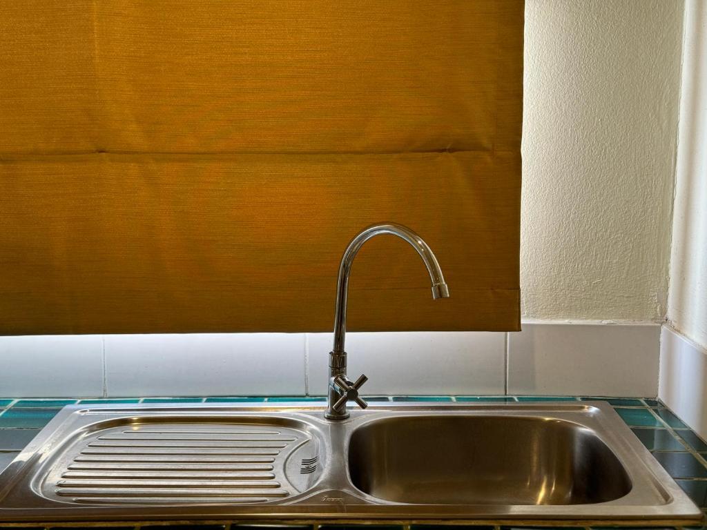A compact stainless-steel kitchen sink beneath a lowered window blind.