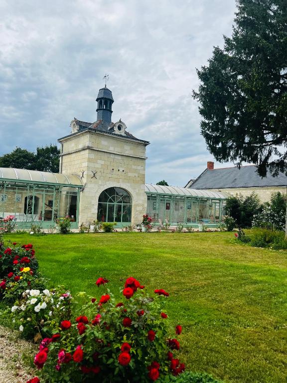un bâtiment avec une tour d'horloge dans une cour fleurie dans l'établissement Château de la Thibaudière - Chambre des oiseaux, à Allonnes