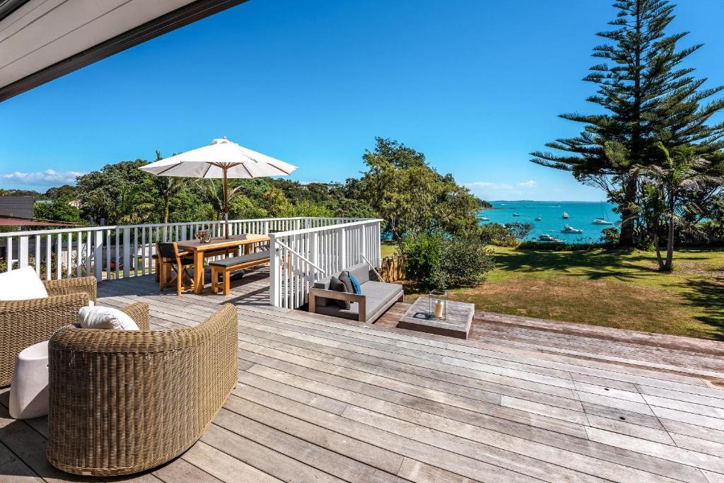 une terrasse avec des chaises, une table et un parasol dans l'établissement Picnic Bay Vista - Be My Guest Waiheke, à Putaki Bay