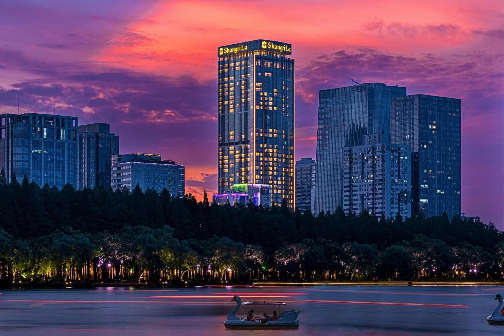 a city skyline at sunset with two boats in the water at Shangri-La Nanjing in Nanjing