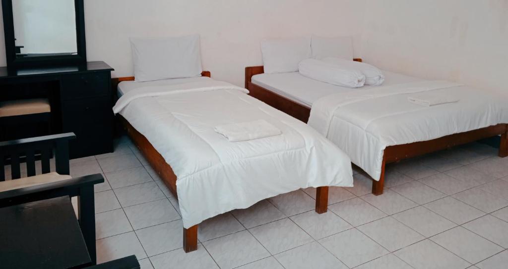 two beds with white sheets in a room at Hotel Wisata in Labuan Bajo
