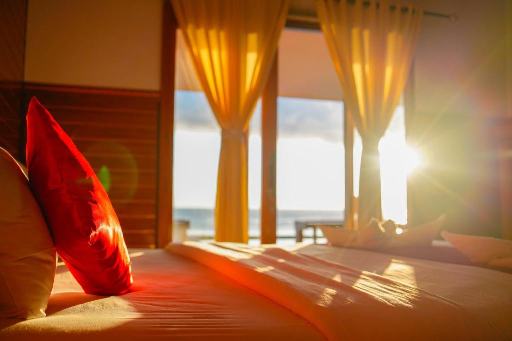a bedroom with a bed with red pillows and windows at DESILA Beach House in Nusa Penida