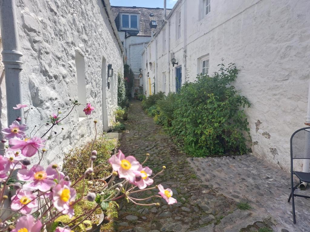 an alley with pink flowers next to white buildings at Blue Door - Kirkcudbright in Kirkcudbright