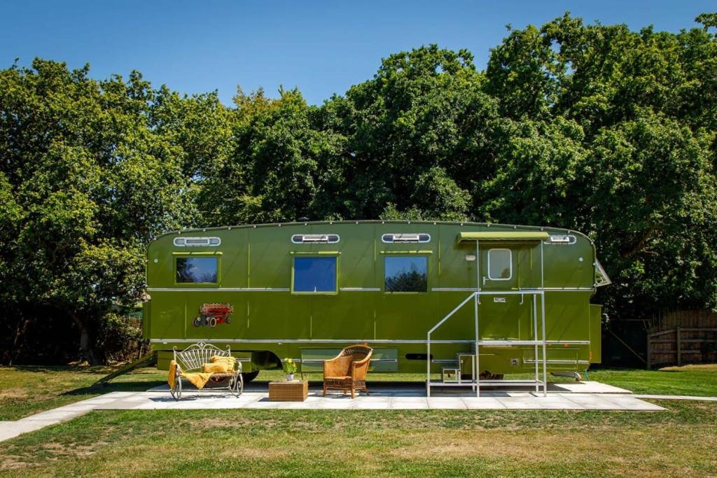 a green trailer parked in a field with two chairs at The Showman's Carriage w King Bed close to beach in Birdham