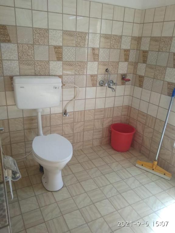 a bathroom with a toilet and a red bucket at Kunsal Yourdum Homestay Ladakh by LexStays in Leh