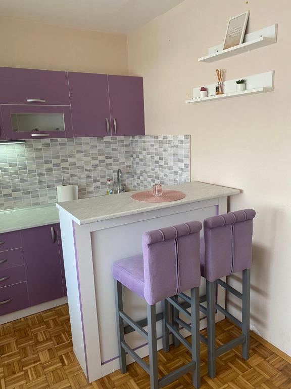 a kitchen with purple cabinets and a counter with purple stools at Niki Apartman in Kruševac