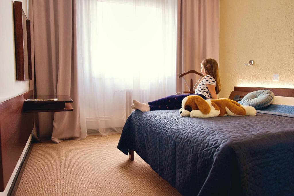 a little girl sitting on a bed with a stuffed animal at Hotel Merkur - Jablonec nad Nisou in Jablonec nad Nisou