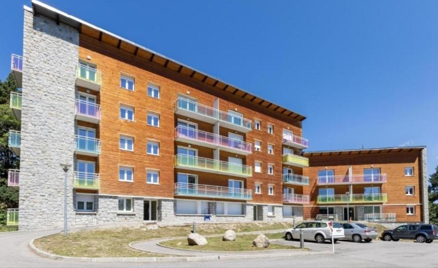 un grand bâtiment en briques avec des voitures garées dans un parking dans l'établissement Panoramic Campus, à Font-Romeu-Odeillo-Via