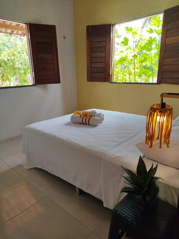 a bedroom with a bed with white sheets and two windows at Villa dos Coqueirais in Icaraí