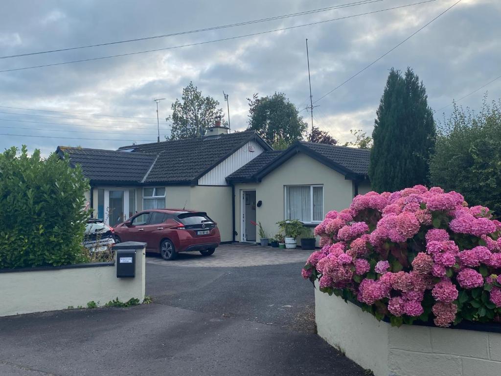 a house with a car parked in a parking lot with pink flowers at Kilmactrasna Cottage in Carrickmacross
