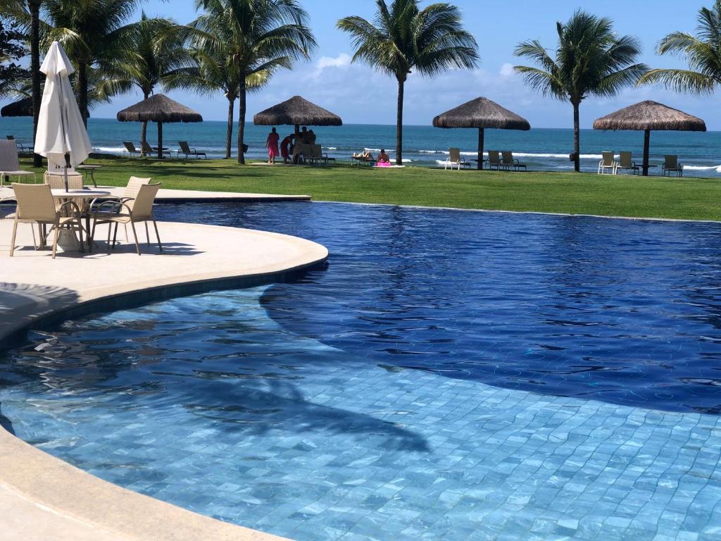 ein Swimmingpool mit Liegen und Sonnenschirmen und das Meer in der Unterkunft Paraíso dos corais Pe na areia in Guarajuba