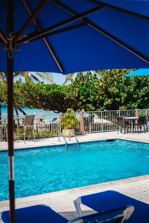 a swimming pool with a blue umbrella and chairs at Coconut Court Beach Hotel in Bridgetown