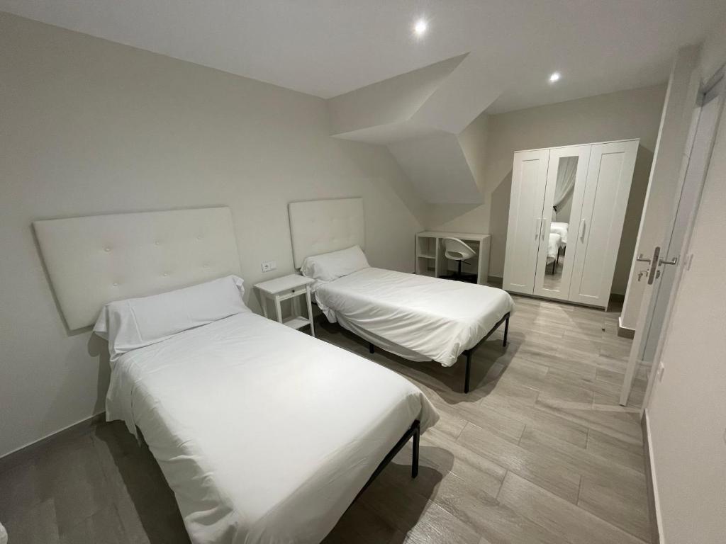 two beds in a room with white walls and wooden floors at Camiño da Camposa in Muxia