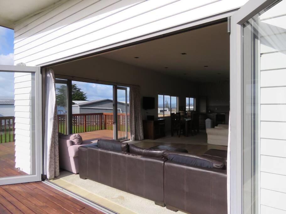 an open patio door with a couch on a deck at Cleggs Batch in Karikari Peninsula