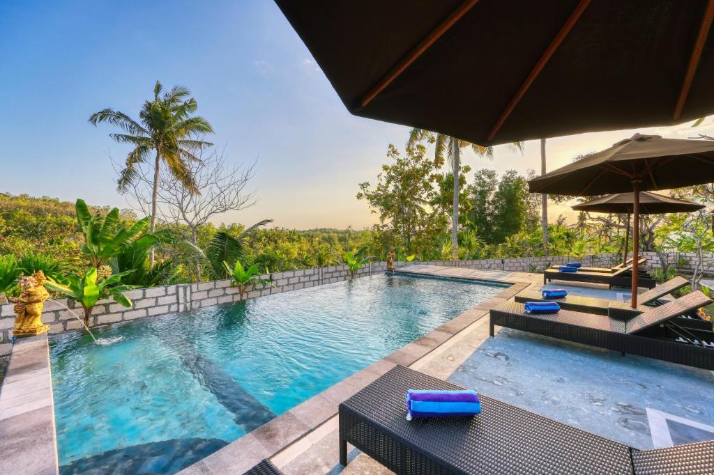 an outdoor swimming pool with chairs and an umbrella at MT Penida Bungalow in Nusa Penida