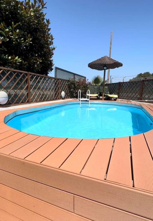 a swimming pool with a wooden deck and an umbrella at O CANTINHO DA RIA - JACUZZI with water at 35 degrees and POOL in Torreira