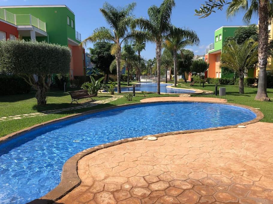 una piscina en un parque con palmeras y edificios en Apartamento Casa Capricho en El Verger Denia, en El Verger