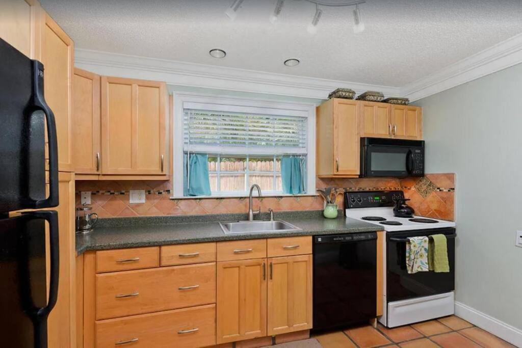 Una cocina con gabinetes de madera y un refrigerador negro. en NEW Beach Quinta 2bed 2 bath Beautiful Yard Tranquility, en Lake Worth