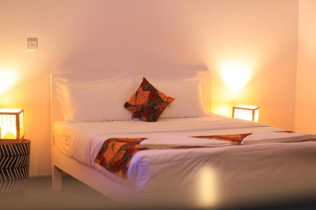 a bedroom with a bed with white sheets and two lights at KaChai Hotel Fort Portal in Kyarusozi