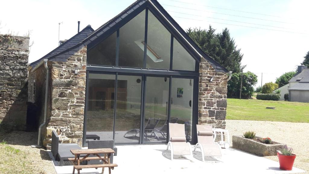 a house with glass doors and a table and chairs at Gîte détente Domaine de Helles -Spa Privatif et Sauna in Poullaouen