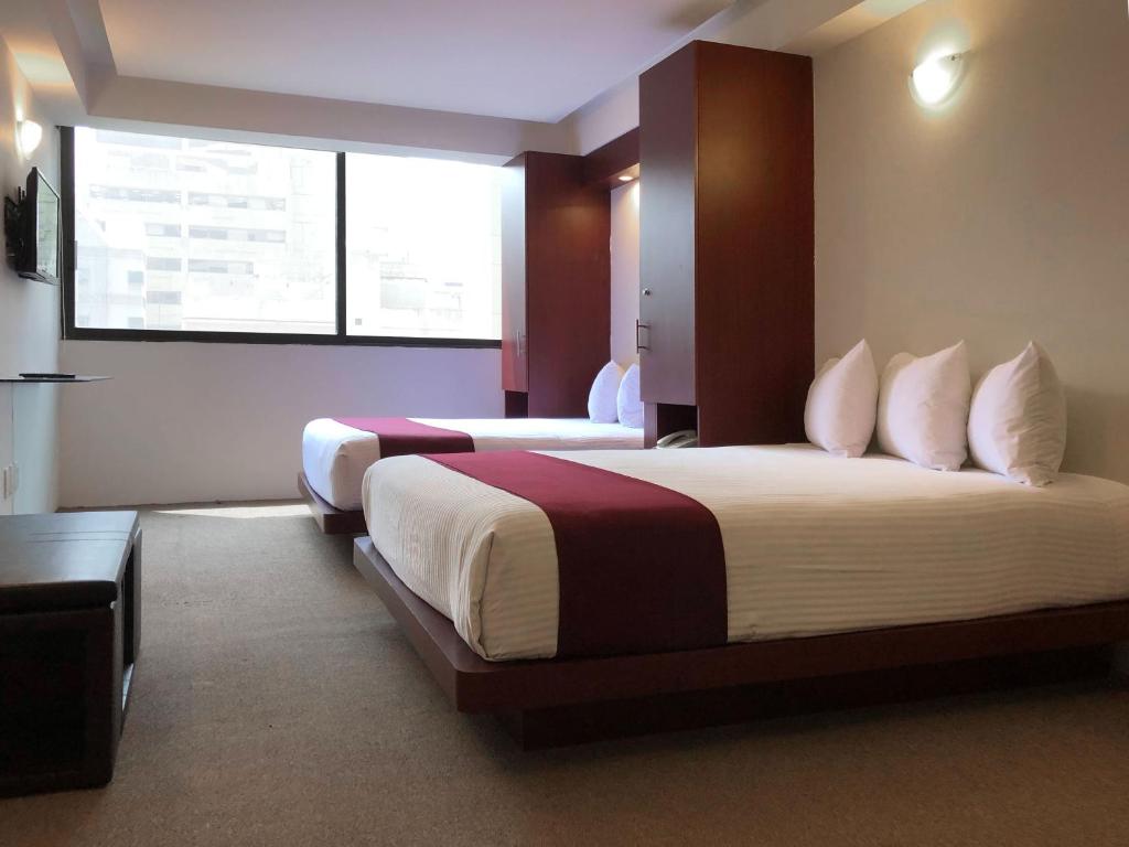 A two-bed room has dark wood storage, wall-mounted television and a large bright window.