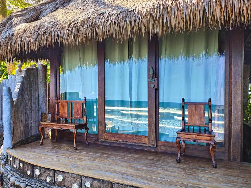 two chairs on a deck with a thatch roof at Beachfront Villa Nixie and the Sea Tabanan in Tabanan