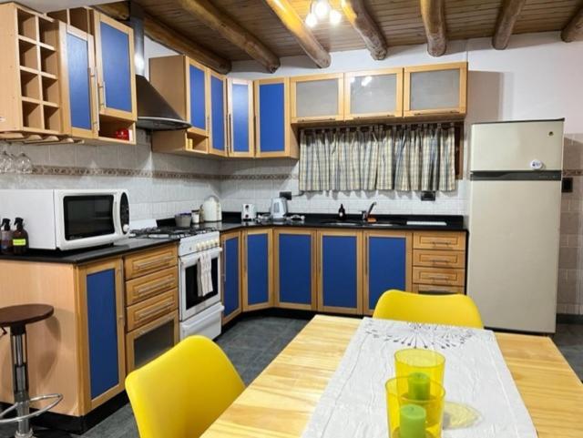a kitchen with blue cabinets and a table and yellow chairs at Casa del Pinar-Plottier-Diario Semanal Mensual-La Mejor Ubicación-Garaje Cerra do in Plottier