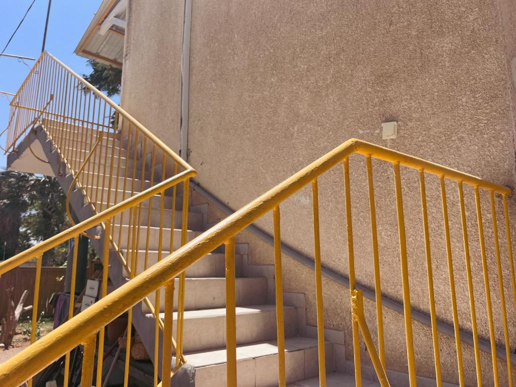 a yellow metal stair railing next to a building at הצימר של יהושע in Ein Gedi
