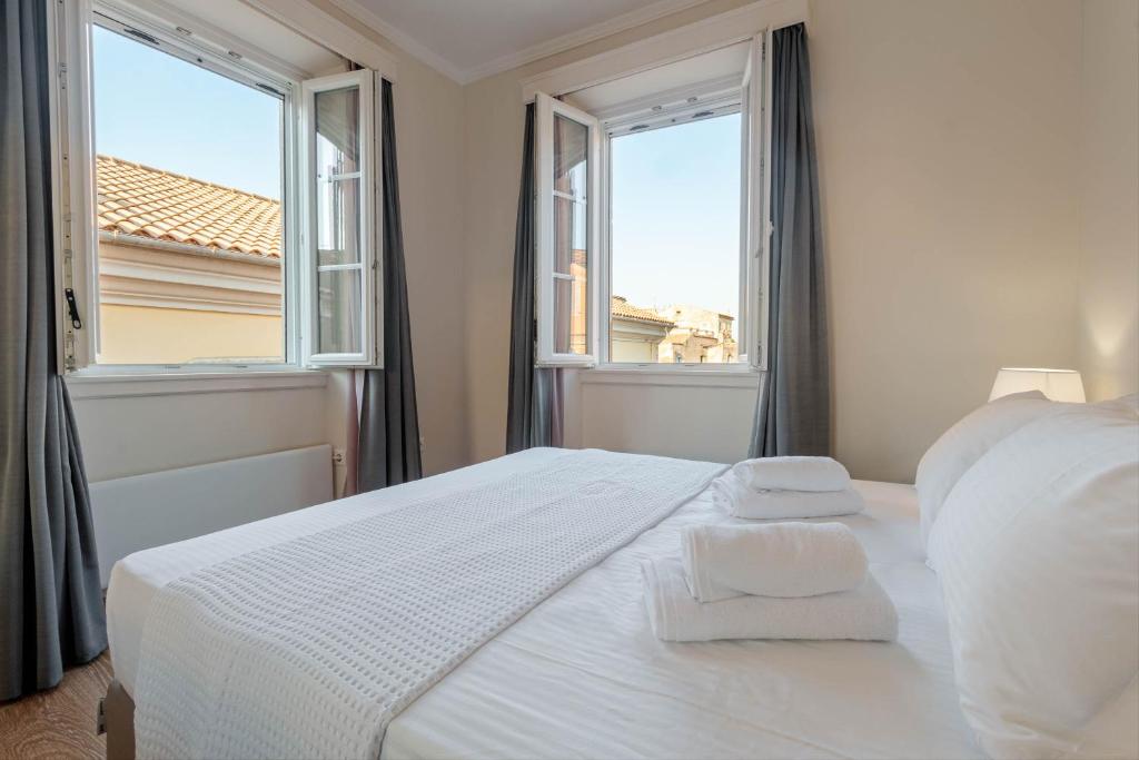 une chambre blanche avec deux serviettes sur un lit et deux fenêtres dans l'établissement The Lucky 12, à Corfu