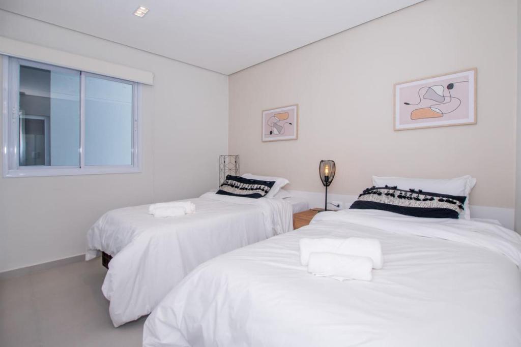 two white beds in a white room with a window at Cityscape Views - New 2BR Retreat in Asuncion